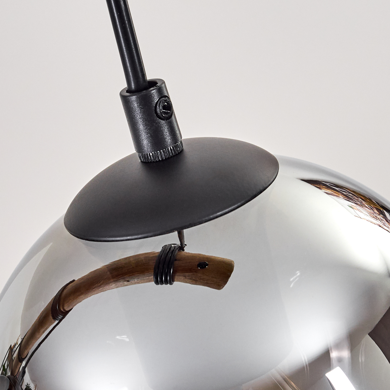 Nahaufnahme einer modernen Pendelleuchte. Sie hat einen schwarzen Metallschaft, eine Glaskugel und ein Holzelement.