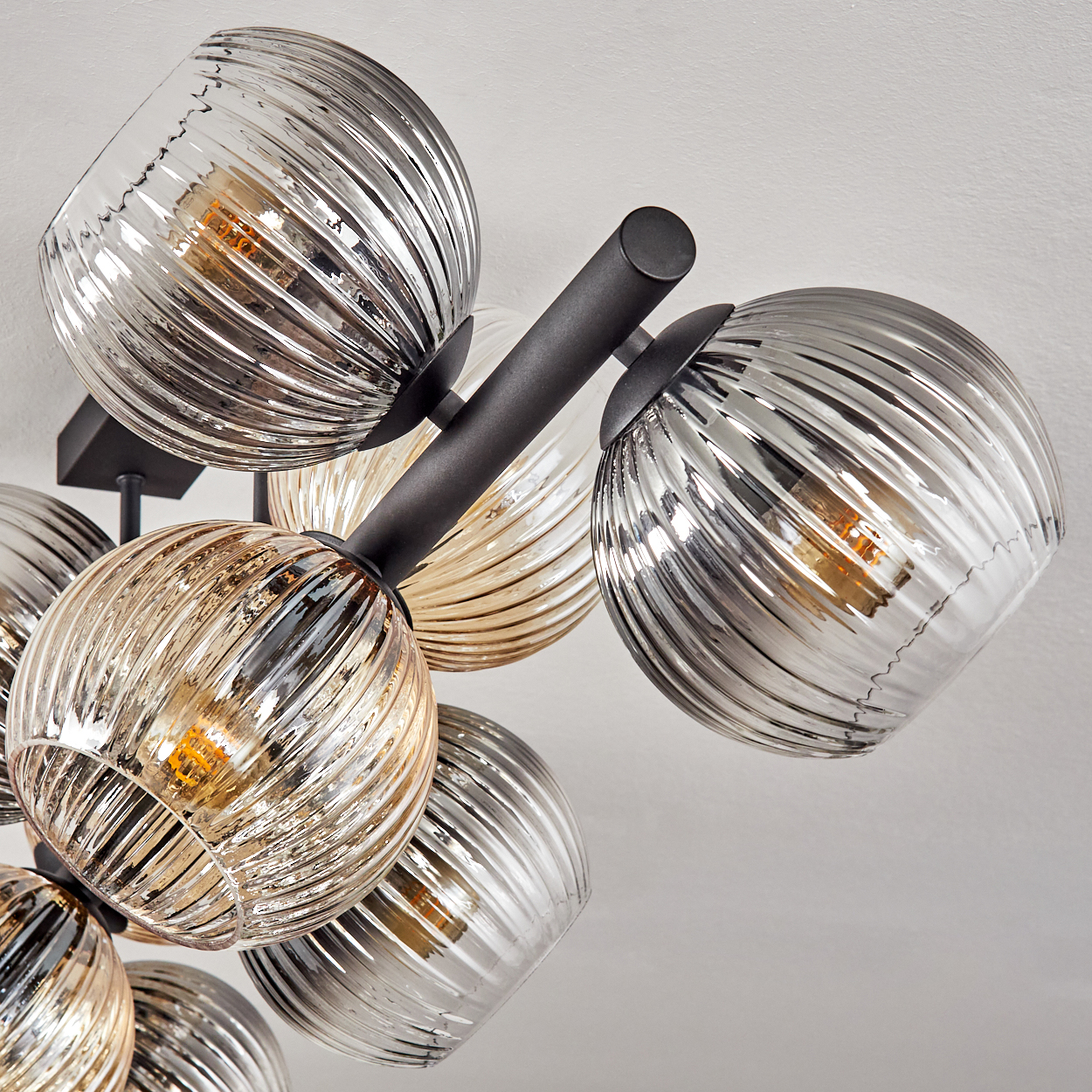 Ein moderner Kronleuchter mit mehreren kugelförmigen Glasschirmen in Grau- und Bernsteintönen, befestigt an schwarzen Metallarmen.