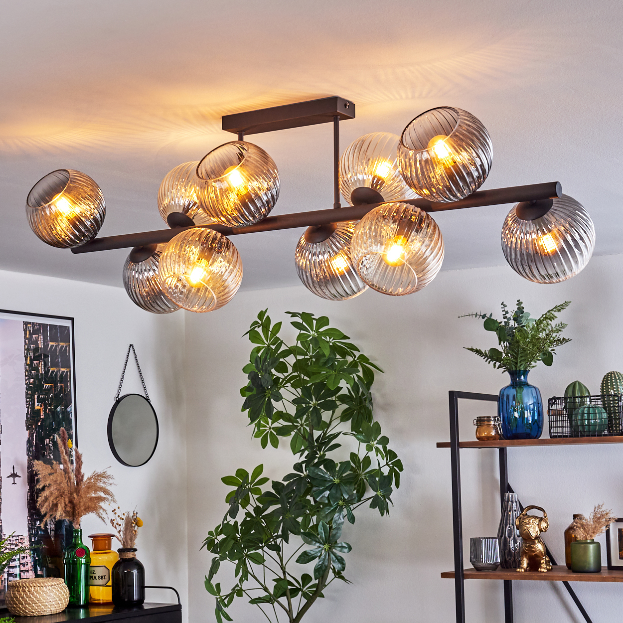Eine moderne Deckenlampe mit Glaskugeln hängt in einem Raum mit Pflanzen, Regalen und einem Spiegel.