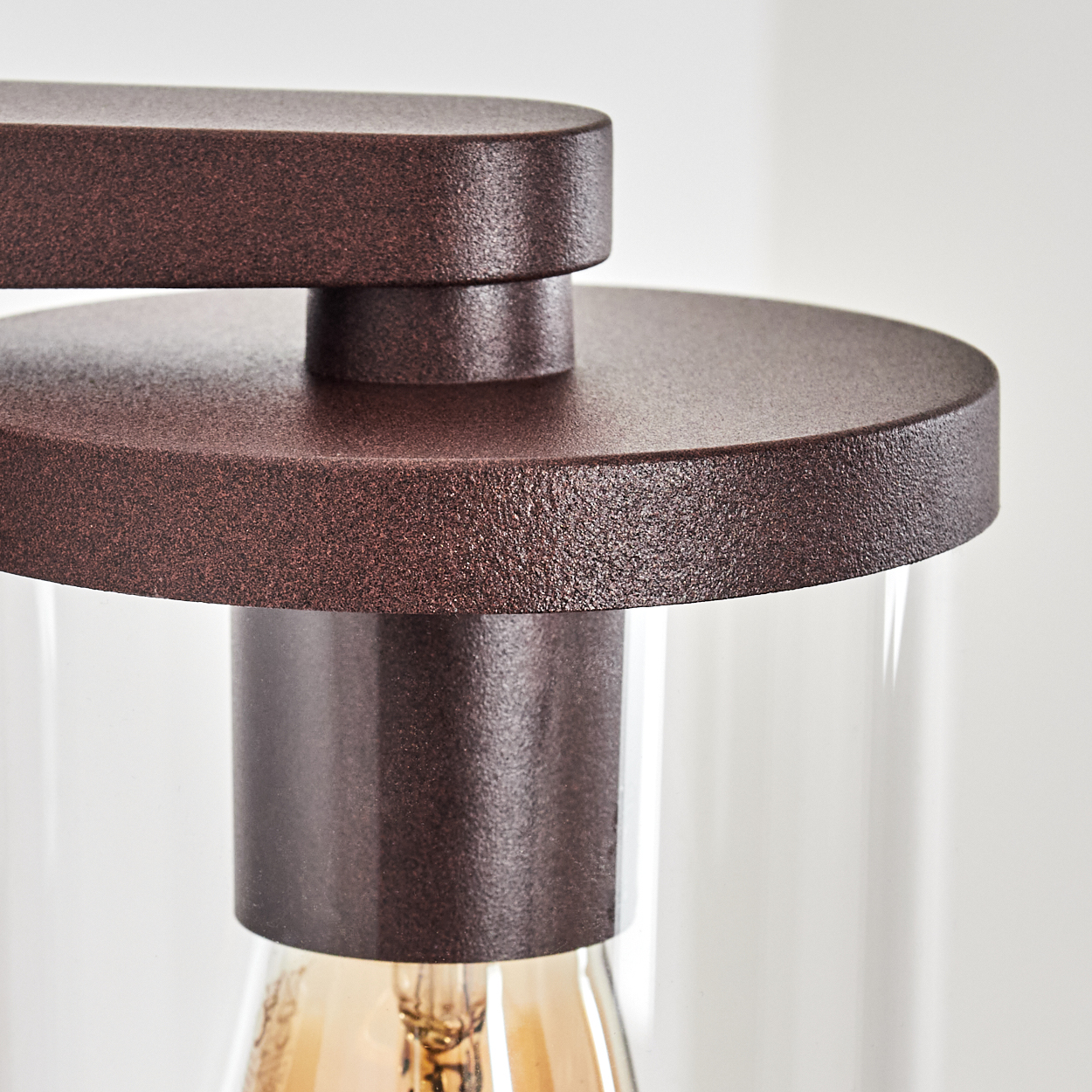 Nahaufnahme einer Lampe. Braune Metallkomponenten über einem Zylinder aus klarem Glas. Unten ist eine Glühbirne zu sehen.
