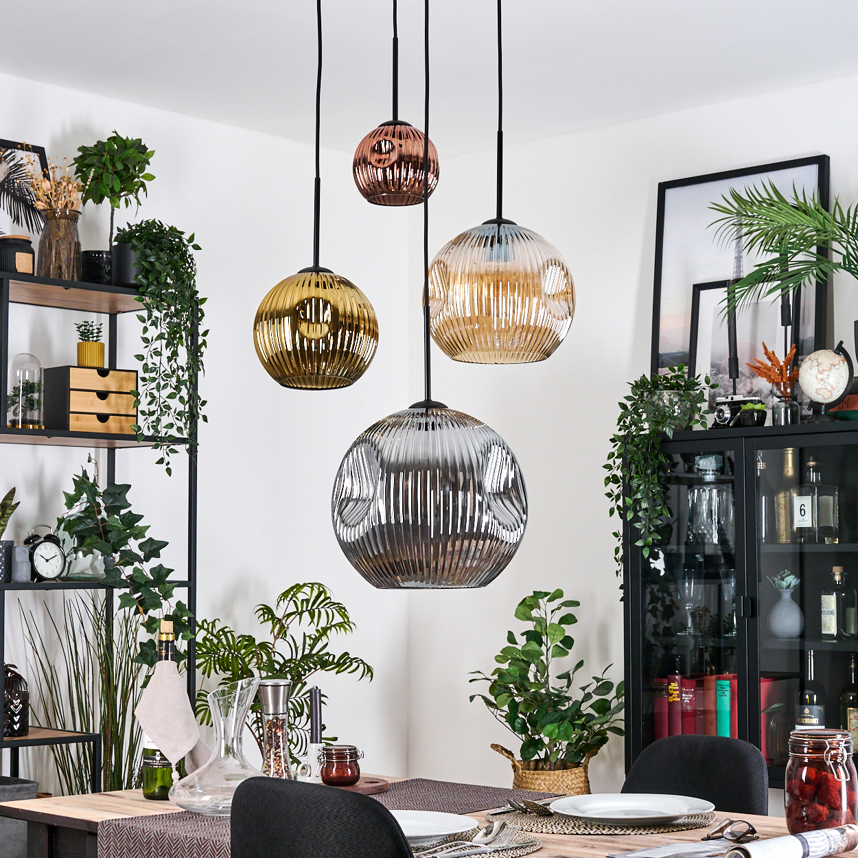 Esszimmer mit hängenden Glaslampen. Regale, Pflanzen und ein Tisch mit Gedeck sind sichtbar. Der Raum ist gut beleuchtet.