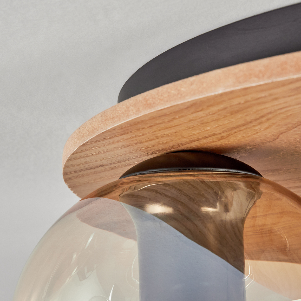 Nahaufnahme einer Deckenleuchte. Sie hat einen kreisförmigen Holzsockel, einen schwarzen Deckel und einen Glasschirm.