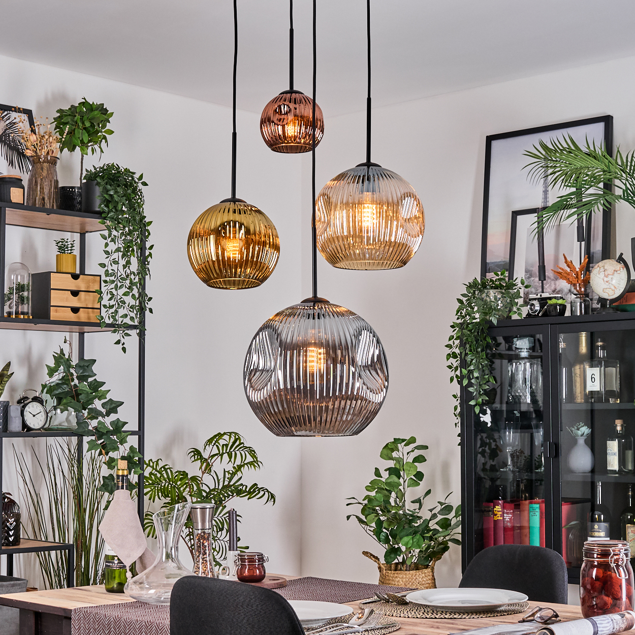 Esszimmer mit hängenden Glaslampen. Pflanzen, Tischgedeck und schwarze Schränke sind im Hintergrund zu sehen.