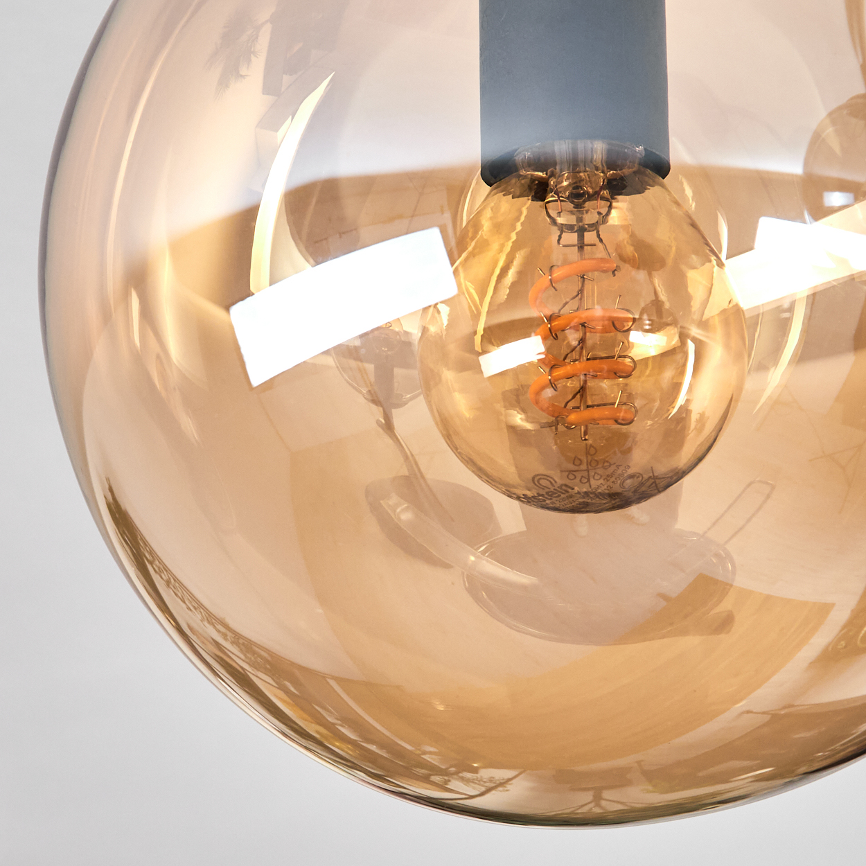 Nahaufnahme einer Leuchte. Ein runder, bernsteinfarbener Glasschirm umgibt eine beleuchtete, orangefarbene Glühbirne.
