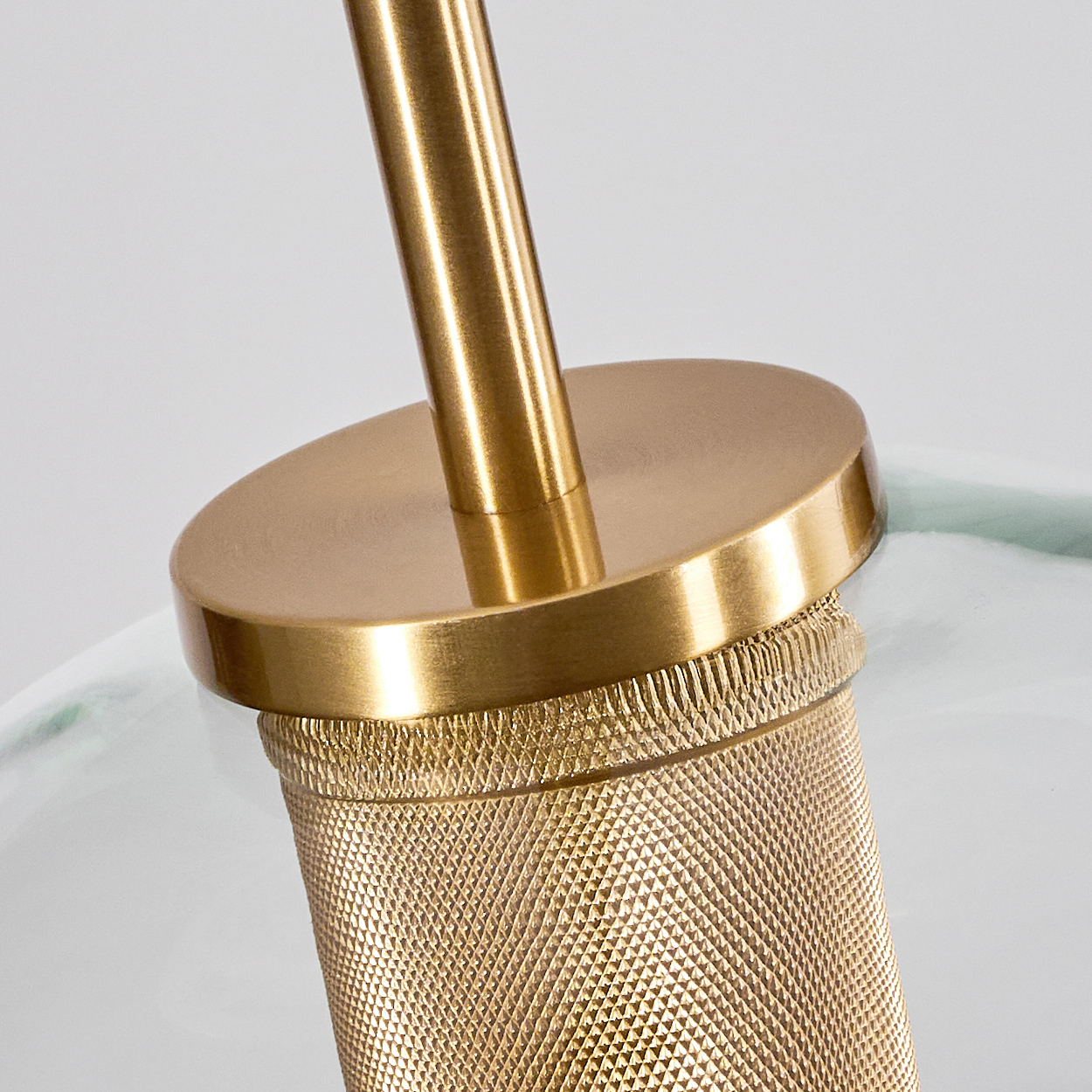 Nahaufnahme eines goldenen Lampenfußes mit strukturierter Grifffläche. Ein zylindrisches Metallteil verbindet sich mit einer kreisförmigen Basis und einer geraden Stange.