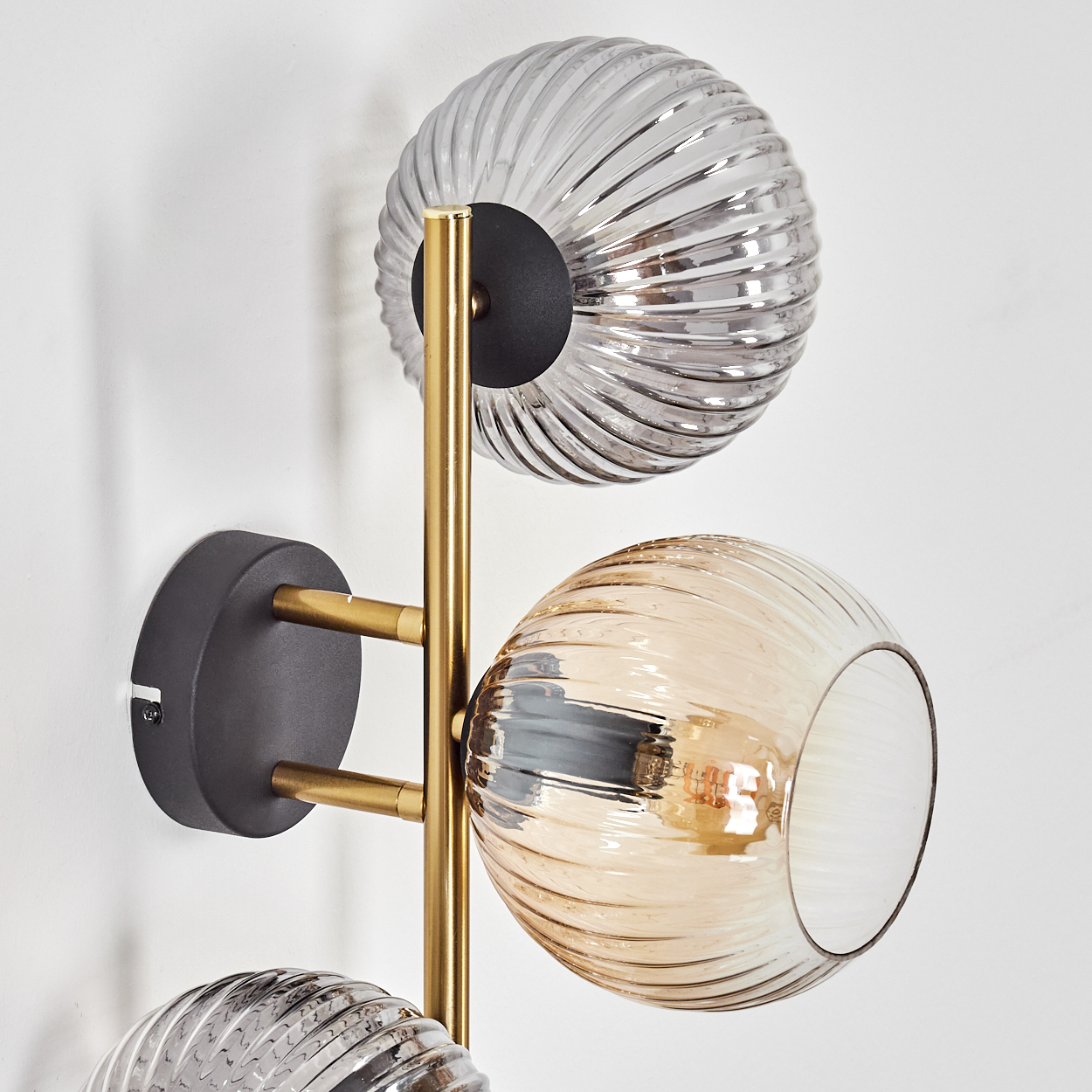 Moderne Wandleuchte mit drei Glaskugeln. Die Kugeln sind gerippt und haben Gold- und Silbertöne. Die Lampe hat einen goldenen Rahmen.