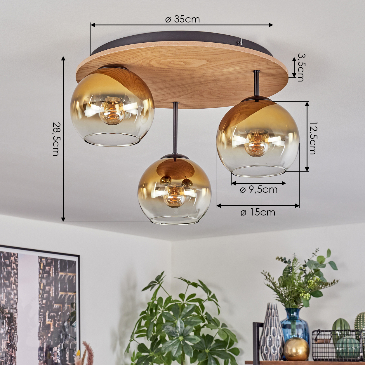 Deckenlampe mit drei Glaskugeln. Braune Holzbasis. Abmessungen sind angegeben. Dekorative Gegenstände im Hintergrund.
