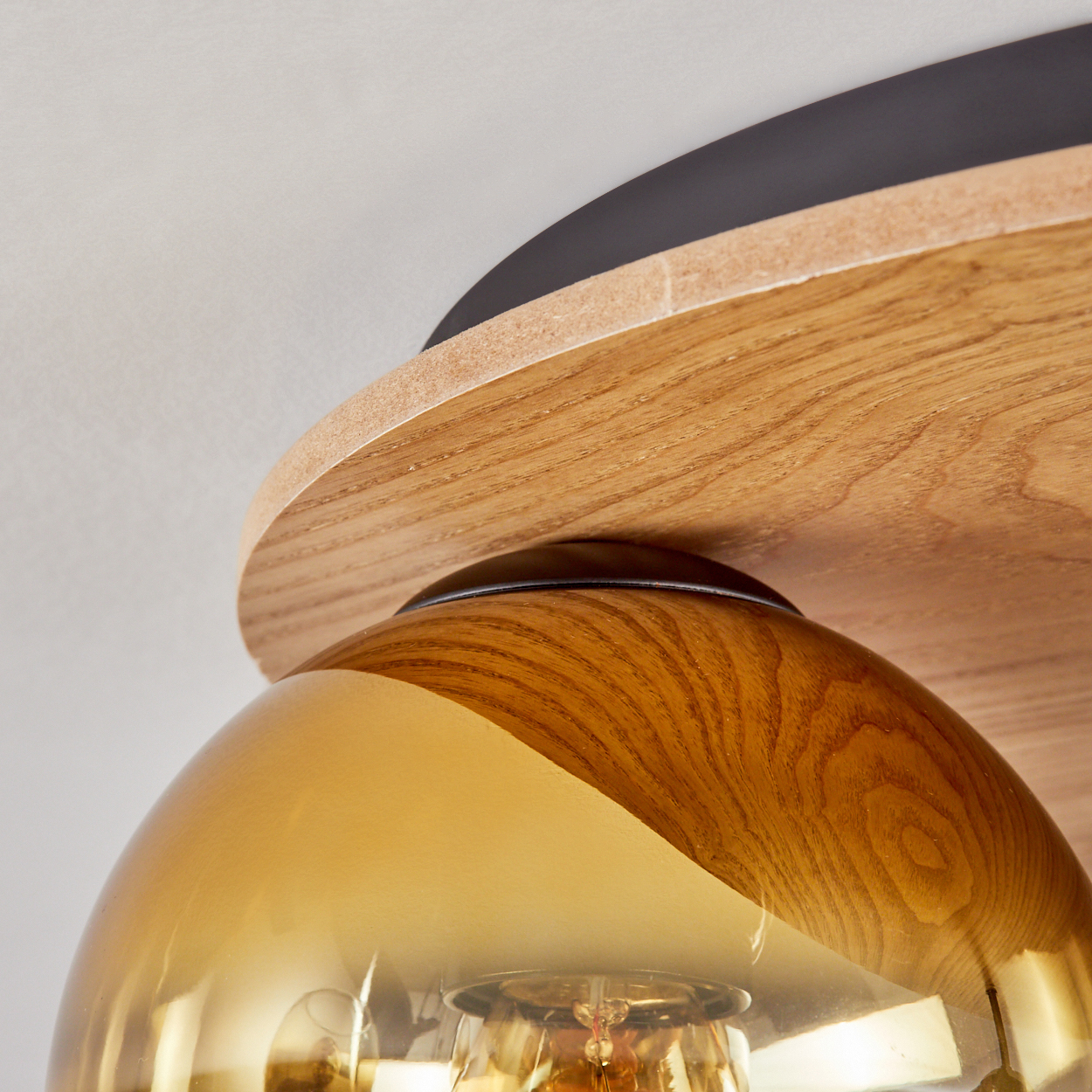 Nahaufnahme einer Deckenlampe. Sie hat einen Holzsockel, einen schwarzen Rand und einen goldenen Glasschirm mit einer Glühbirne.