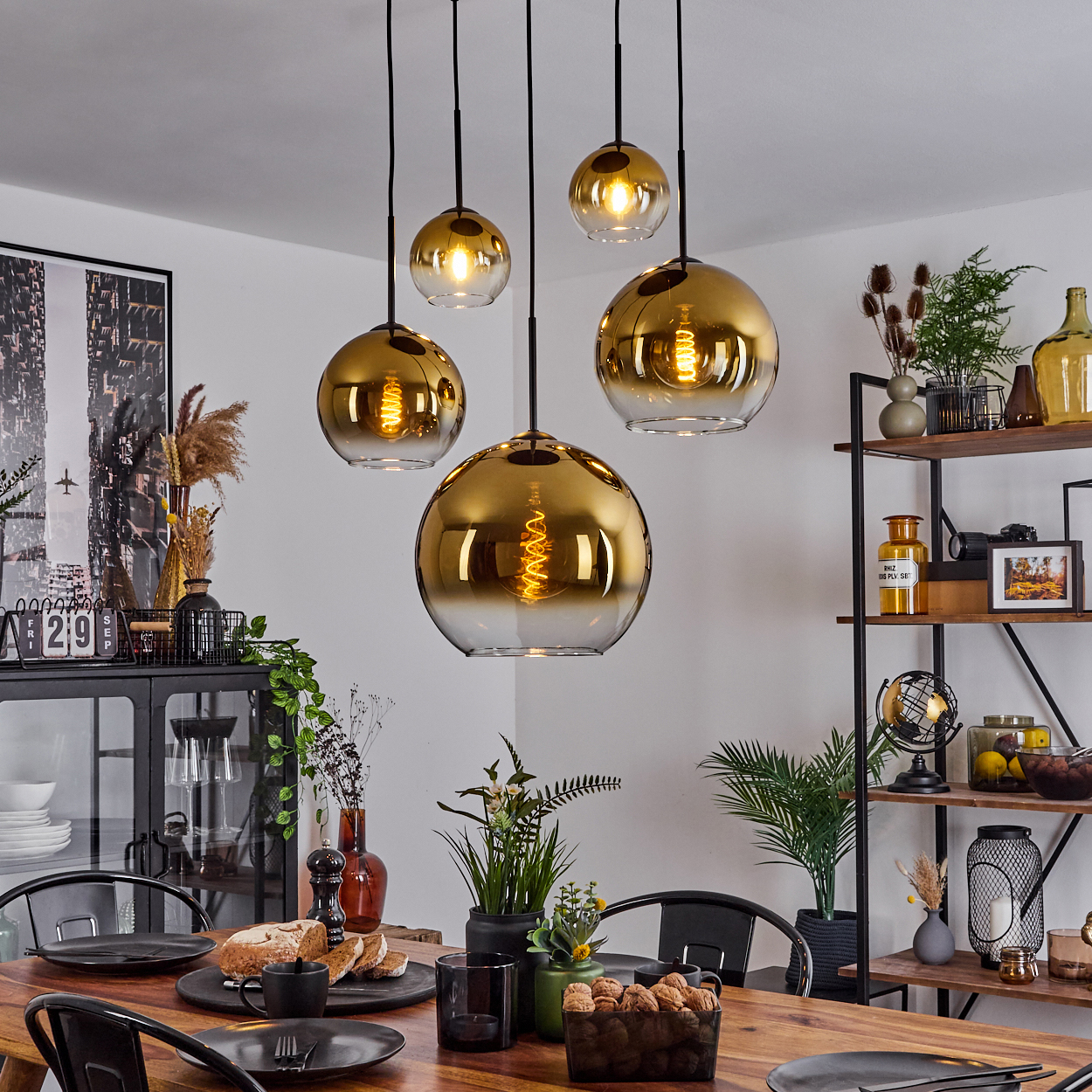 Esszimmer mit Holztisch, schwarzen Stühlen und goldenen Lampen. Auf Regalen und dem Tisch befinden sich Dekorationsartikel.