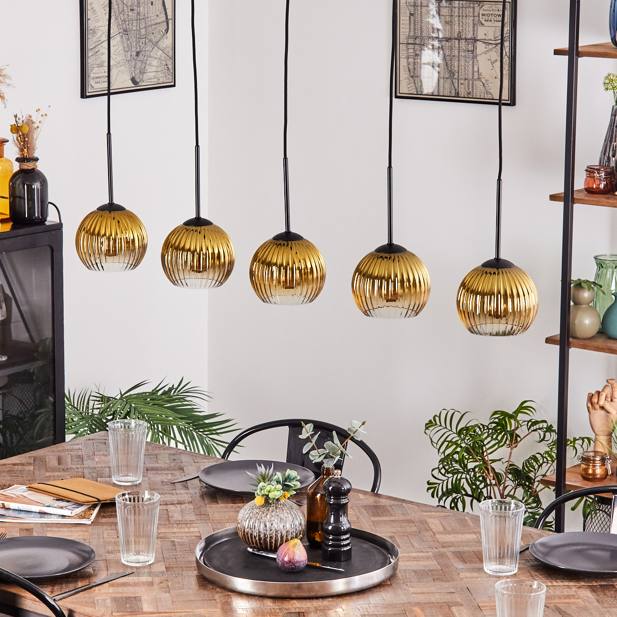 Esszimmer mit Holztisch, fünf goldenen Pendelleuchten und einem schwarzen Tablett mit Dekorationen.