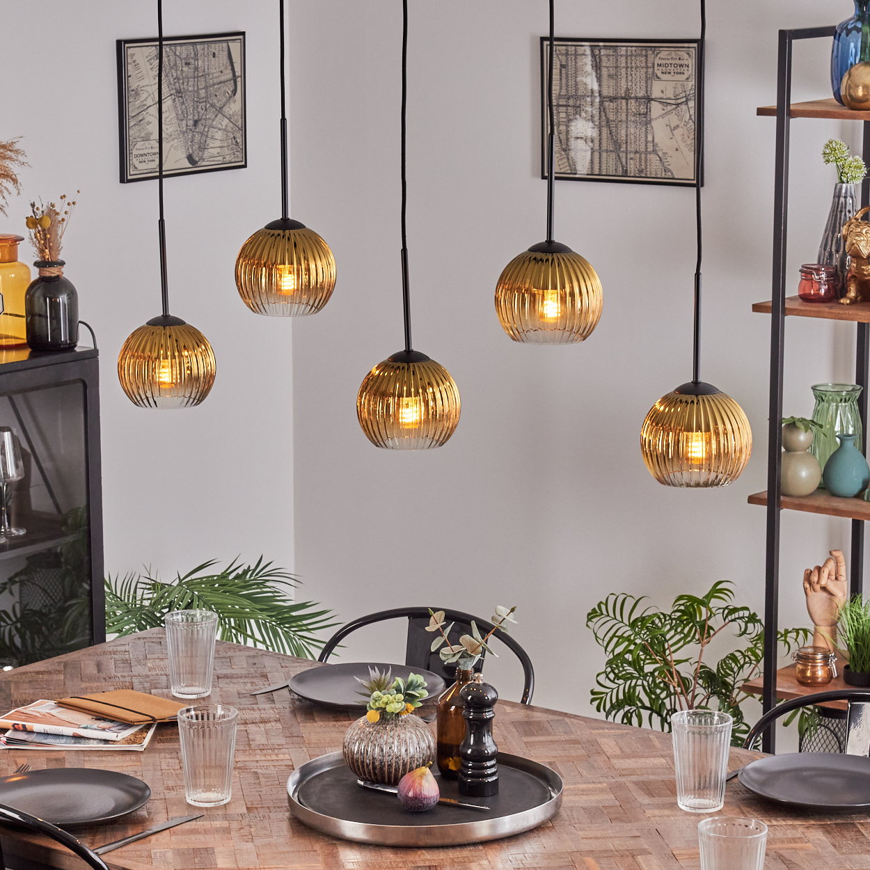 Esszimmer mit Holztisch, Hängelampen, Tellern, Gläsern und Dekorationsartikeln. Regale mit Vasen und Kunstwerken an der Wand.