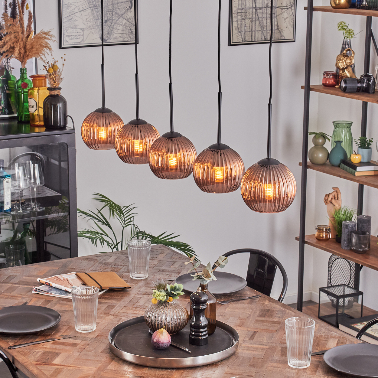 Esszimmer mit Holztisch, Hängelampen und Tischdekoration. Im Hintergrund ein Regal mit Dekoration.