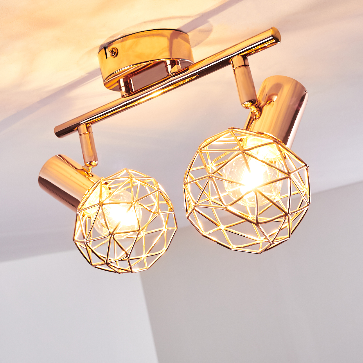Eine moderne, goldfarbene Deckenleuchte. Sie hat zwei kugelförmige Lichtkäfige und Scheinwerfer, die an einer Stange befestigt sind, mit hellen Glühbirnen.
