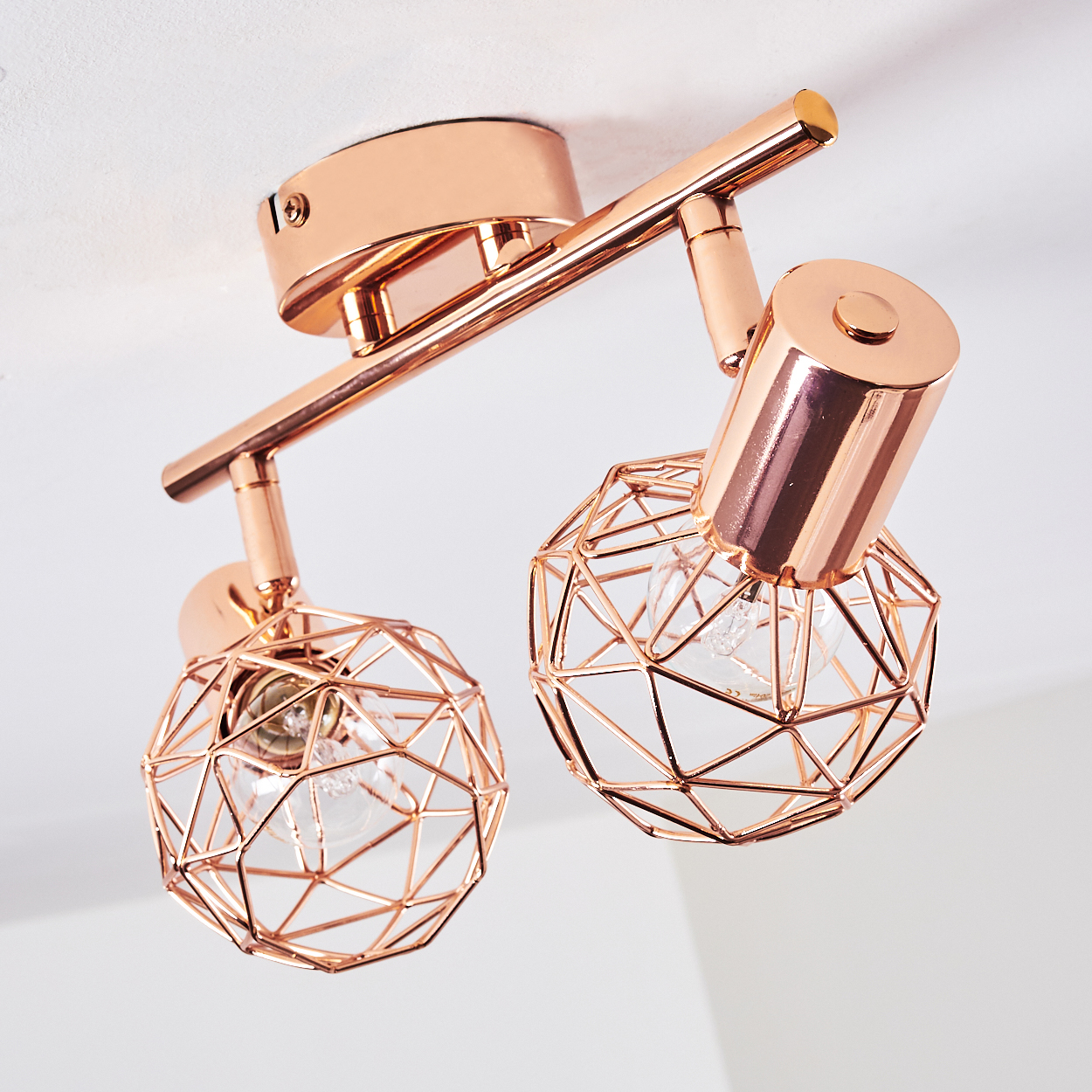 Eine roségoldene Deckenleuchte mit zwei geometrischen Lampenschirmen, die jeweils eine Glühbirne enthalten, vor weißer Decke.