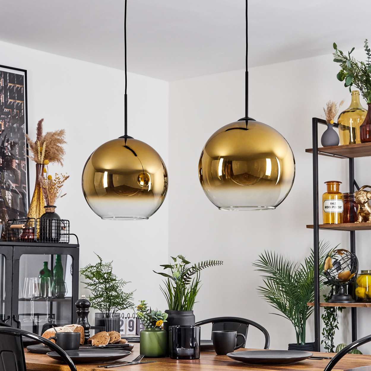 Zwei goldene Pendelleuchten hängen über einem Esstisch, der für eine Mahlzeit gedeckt ist. Der Raum hat ein modernes Design mit dekorativen Elementen.