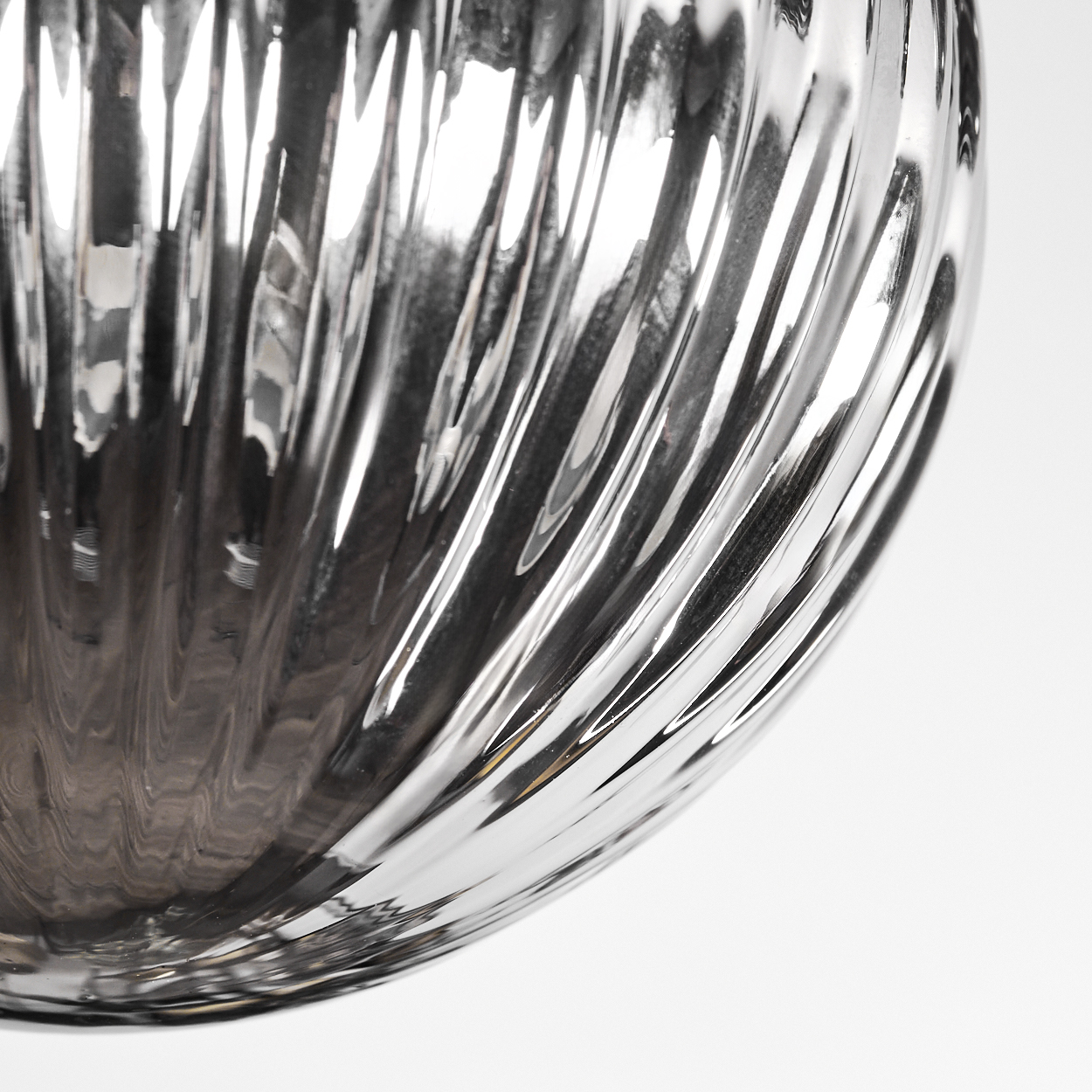 Nahaufnahme eines Glasobjekts mit gerippter Oberfläche. Das Glas reflektiert Licht, wodurch Glanzlichter und Schatten entstehen. Der Hintergrund ist weiß.