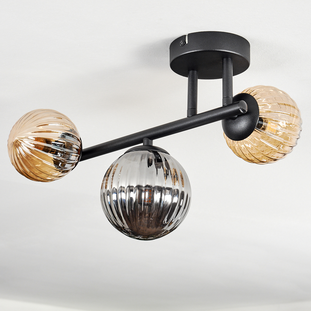 Eine moderne Deckenleuchte mit drei Glaskugeln. Die Kugeln sind bernsteinfarben und silberfarben, mit schwarzen Metallarmen.
