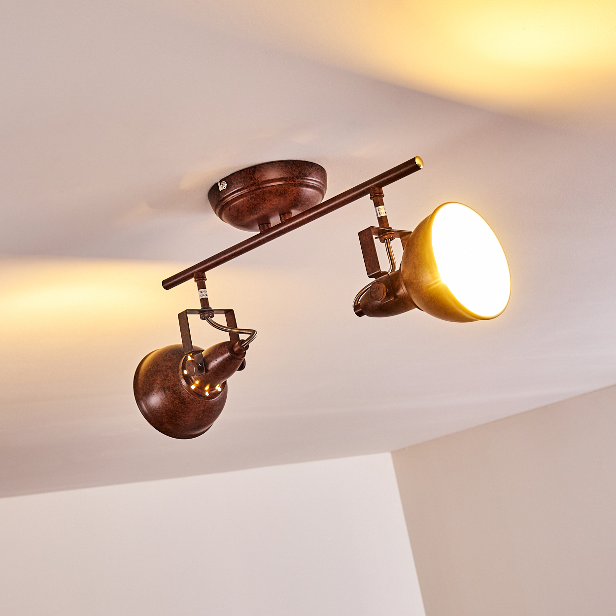 Eine Deckenstrahler-Leuchte mit zwei Lampen. Die Lampen sind braun und beleuchtet, mit einer weißen Decke im Hintergrund.