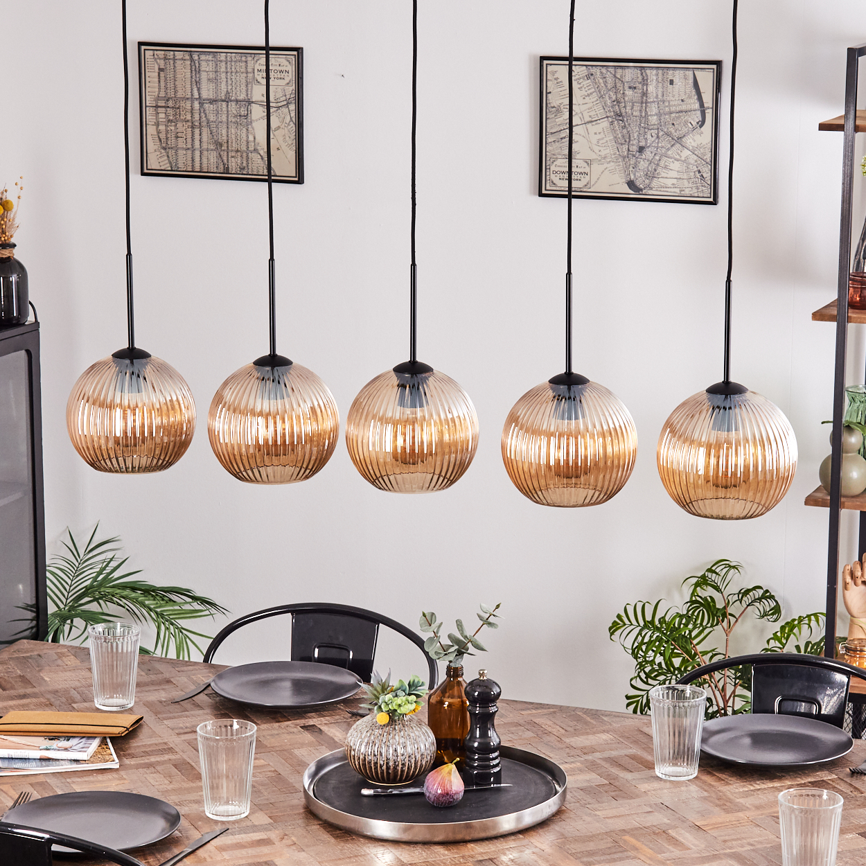 Esszimmer mit Hängelampen, Tisch mit Tellern, Gläsern und Dekoration. Hintergrund: Karten, Pflanzen und Regale.