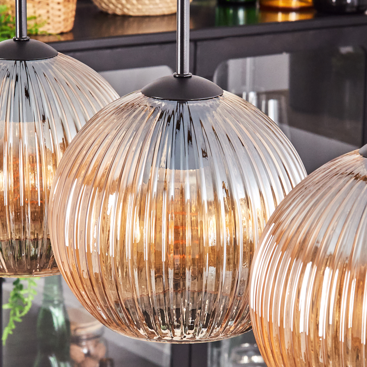 Drei Glas-Pendelleuchten mit geripptem Design. Die Leuchten sind bernsteinfarben und hängen an schwarzen Halterungen.