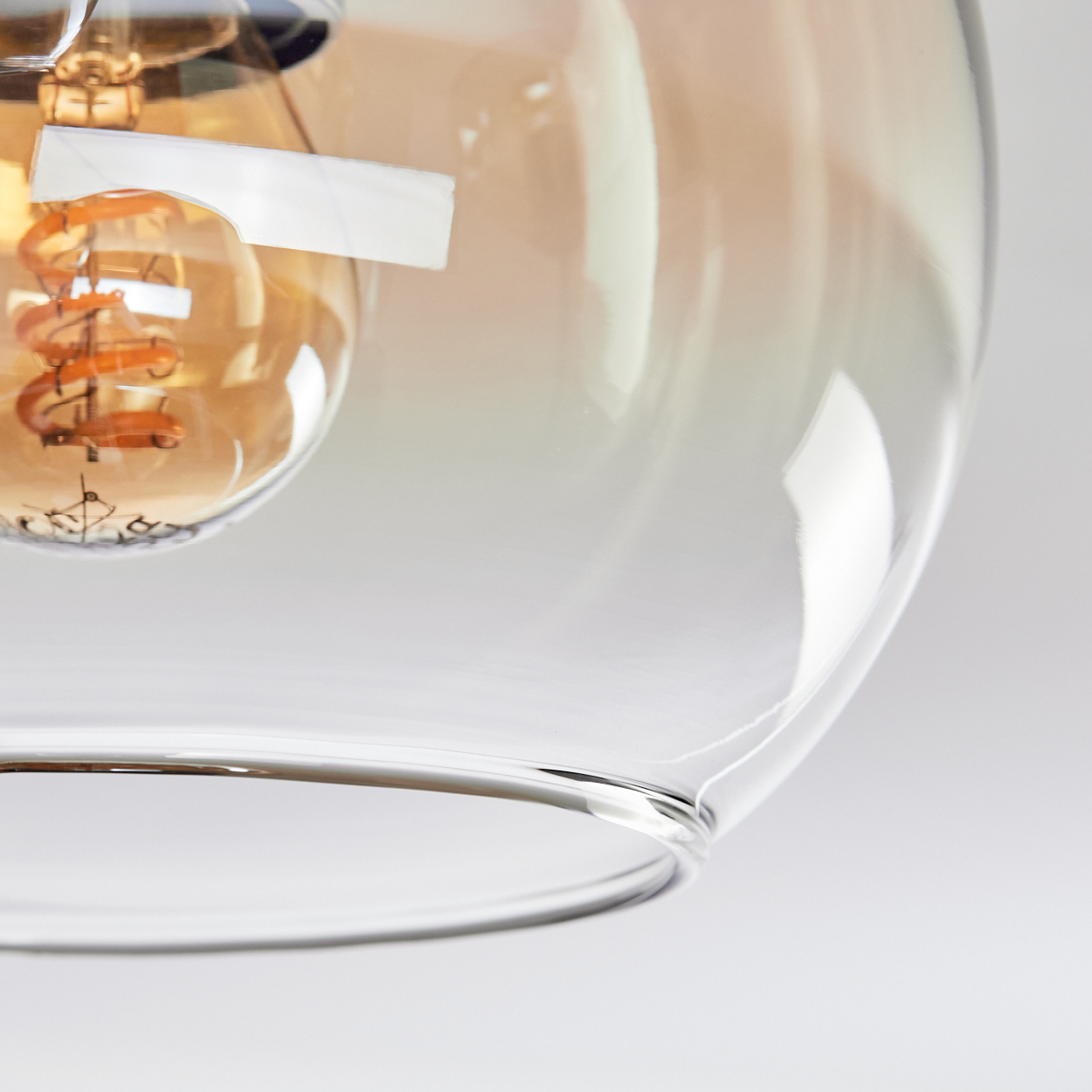 Nahaufnahme eines Glasschirms mit einer sichtbaren Glühbirne. Die Glühbirne hat einen warmen Orangeton und einen sichtbaren Glühfaden.