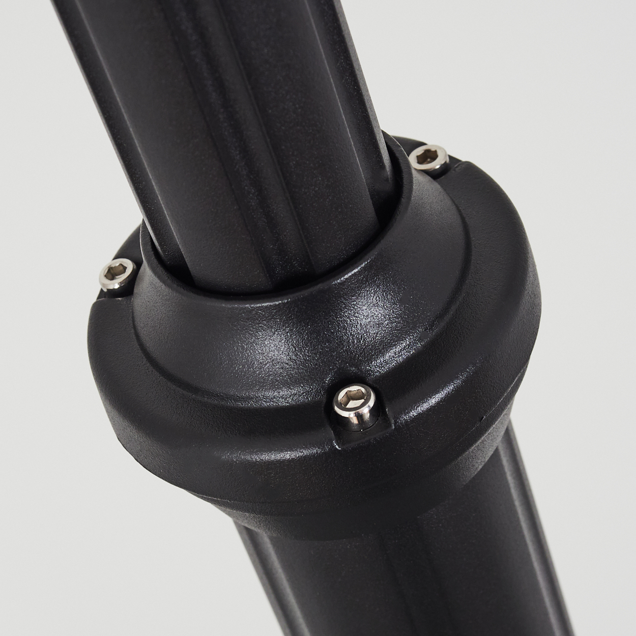 Nahaufnahme eines schwarzen Metallobjekts. Das Objekt hat ein rundes, geripptes Design mit Bolzen. Es ist vor einem schlichten, hellen Hintergrund platziert.