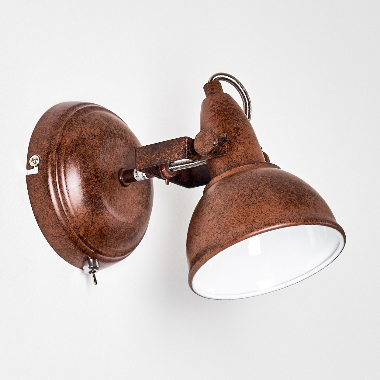Eine bronzefarbene Wandleuchte mit weißem Innenraum. Sie befindet sich an einer weißen Wand. Die Lampe hat einen runden Sockel und einen verstellbaren Kopf.
