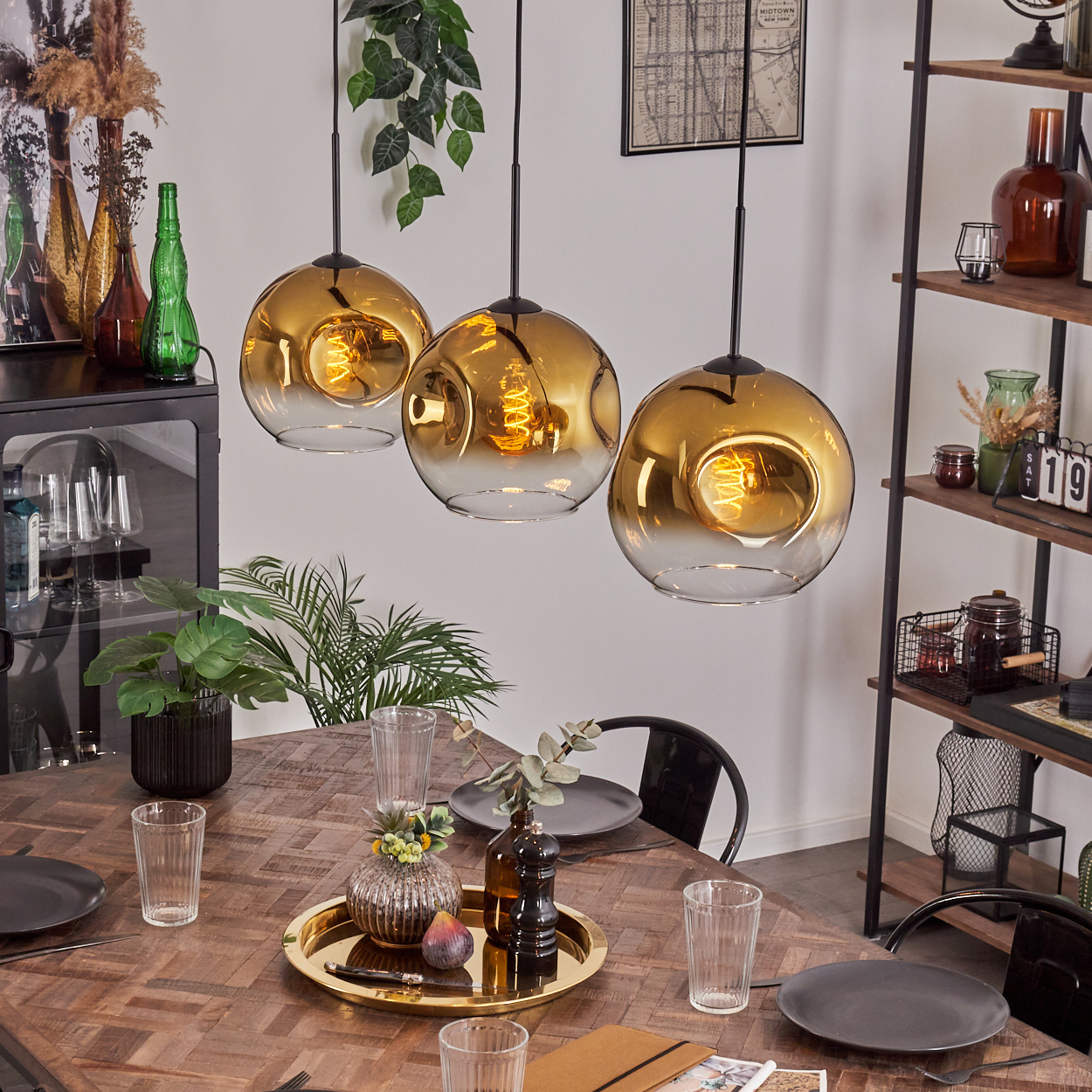 Esszimmer mit drei goldenen Pendelleuchten, einem Holztisch und Dekorationsartikeln auf einem Regal und Tisch.