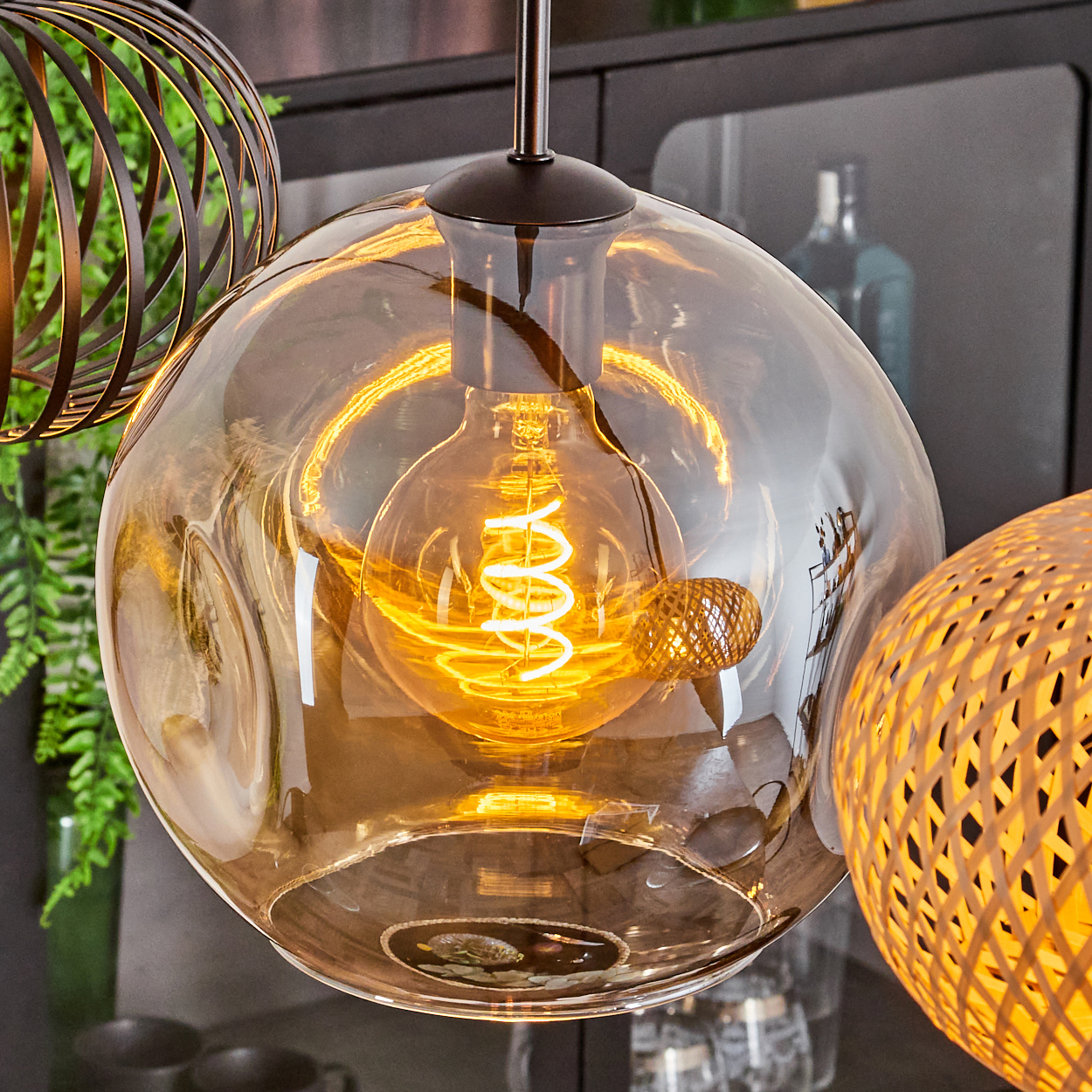 Nahaufnahme einer Pendelleuchte mit großem, klarem Glasglobus. Im Inneren befindet sich ein Spiralfilament. Andere dekorative Lichter sind sichtbar.