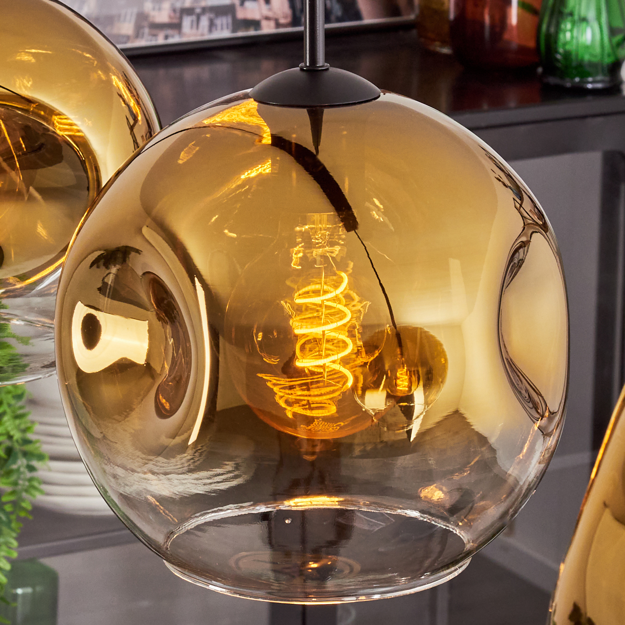 Nahaufnahme einer Glas-Pendelleuchte. Die Lampe hat einen goldenen Glasschirm mit einer Wendelglühbirne.