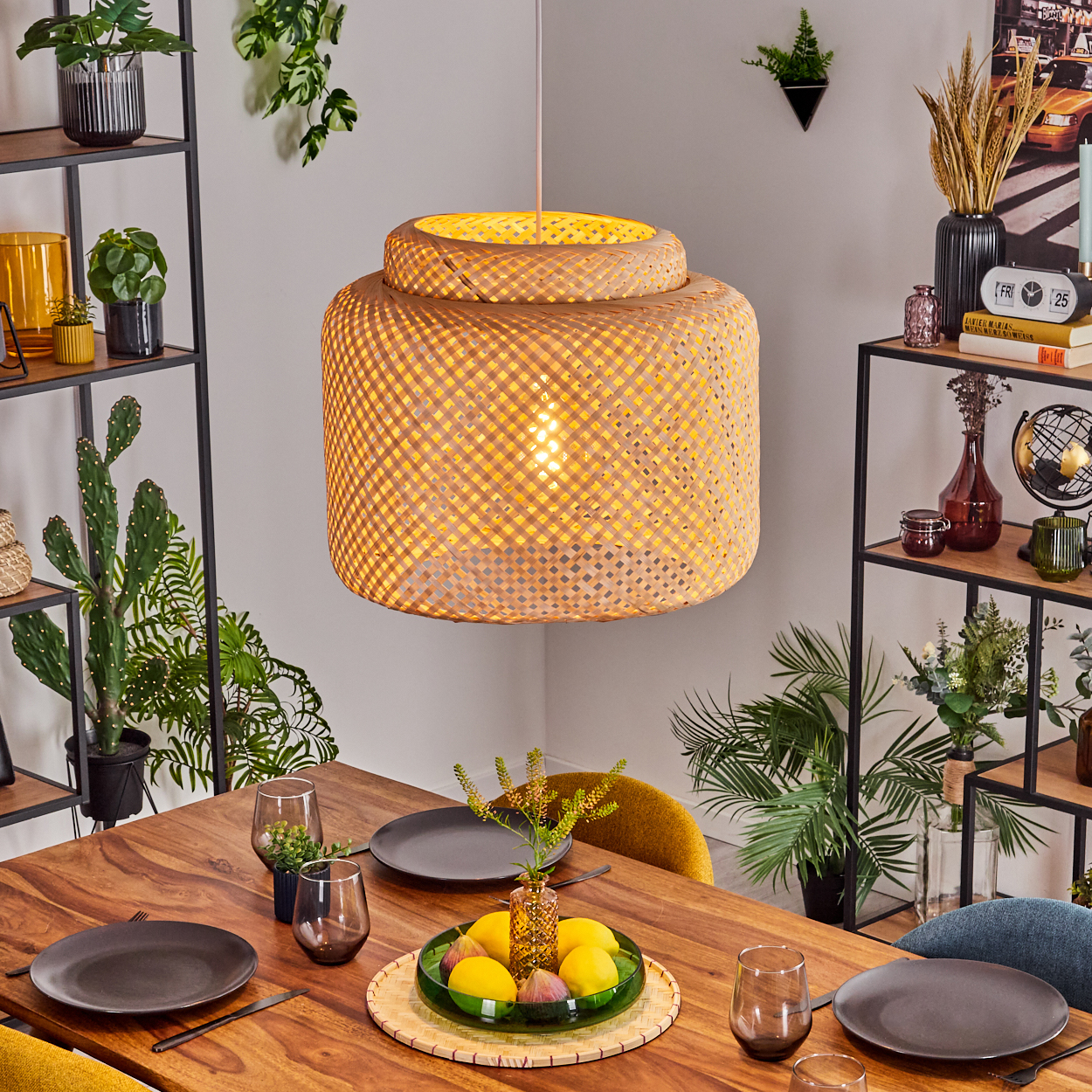 Esszimmer mit Holztisch, gewebter Lampe, Pflanzen, Tellern und Gläsern. Obst und Dekoration stehen auf dem Tisch.