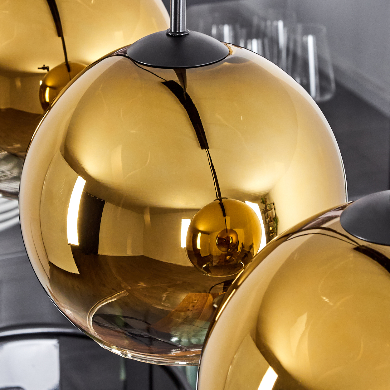 Nahaufnahme von drei goldenen, kugelförmigen Pendelleuchten. Jede hat einen schwarzen Deckel und eine kleine, reflektierende Kugel.
