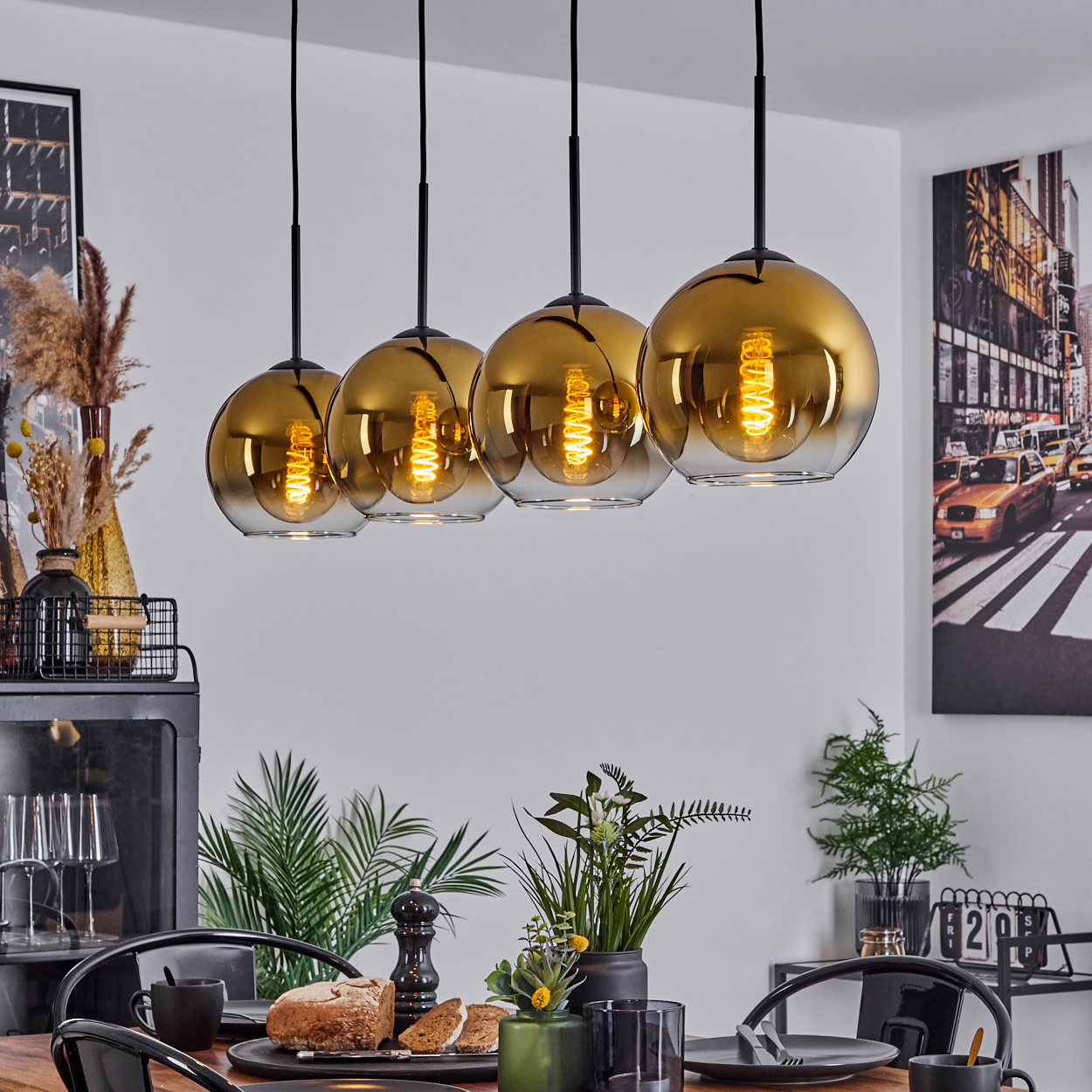 Esszimmer mit goldenen Kugellampen, Tisch mit Brot und Pflanzen, und ein New York City Foto an der Wand.