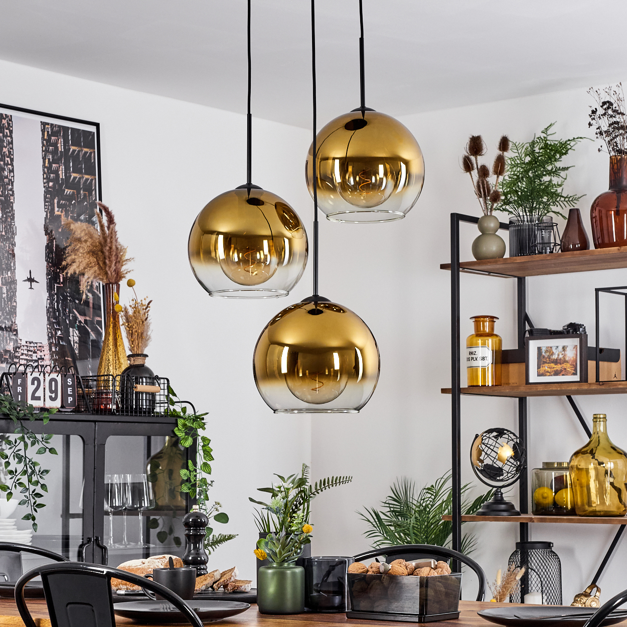 Esszimmer mit drei goldenen Pendelleuchten. Tisch mit Tellern und Essen. Regale mit Dekorationen.