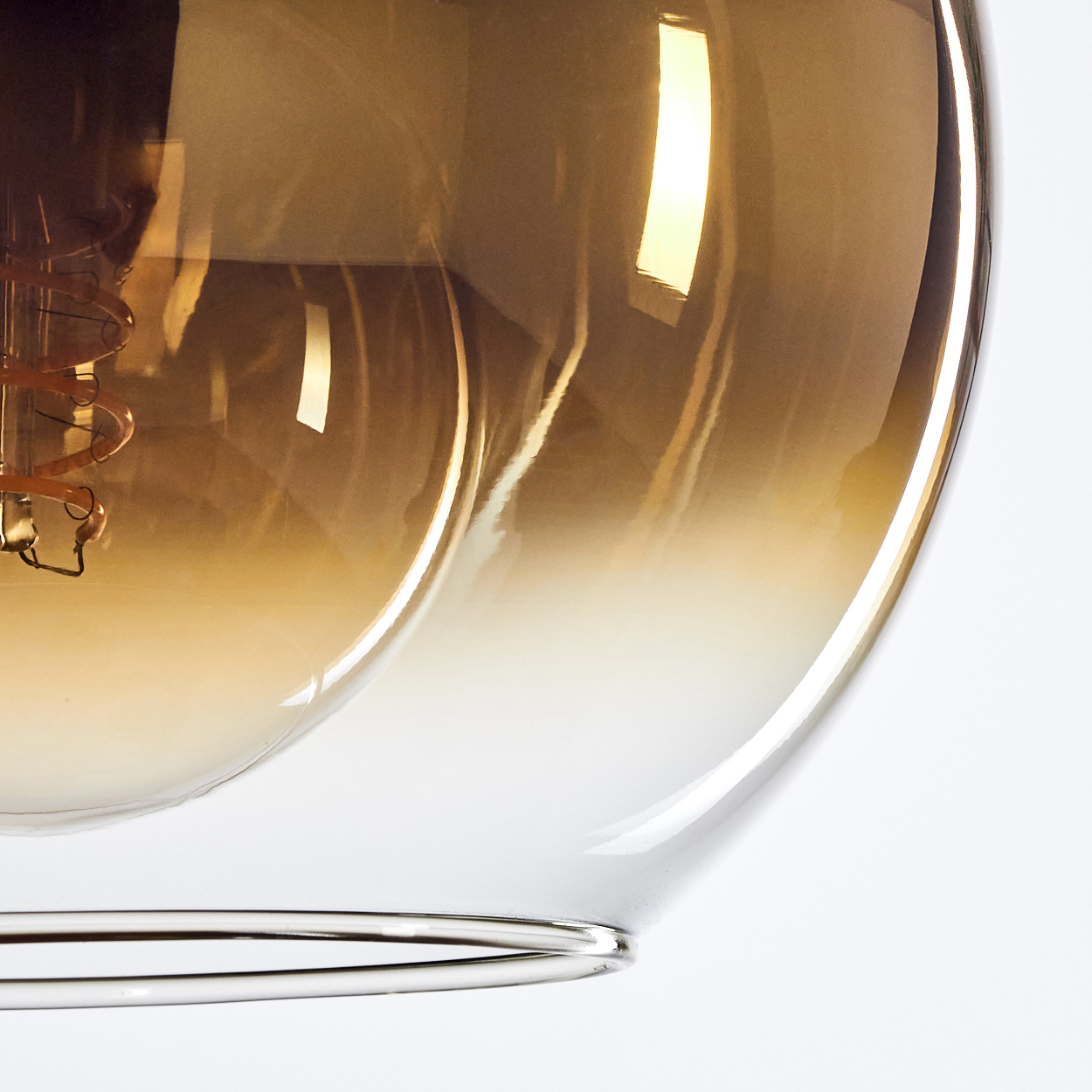 Nahaufnahme einer Leuchte mit einem Glasschirm, der von braun nach klar verblasst. Ein Metallring stützt den Schirm.