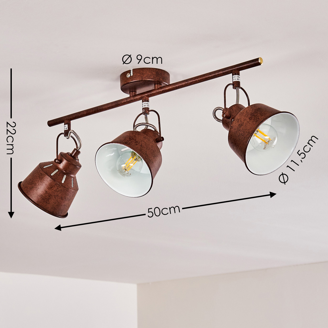 Ein rostbrauner Deckenstrahler mit drei Lampen. Jede Lampe hat einen weißen Innenraum und eine sichtbare Glühbirne. Abmessungen sind enthalten.
