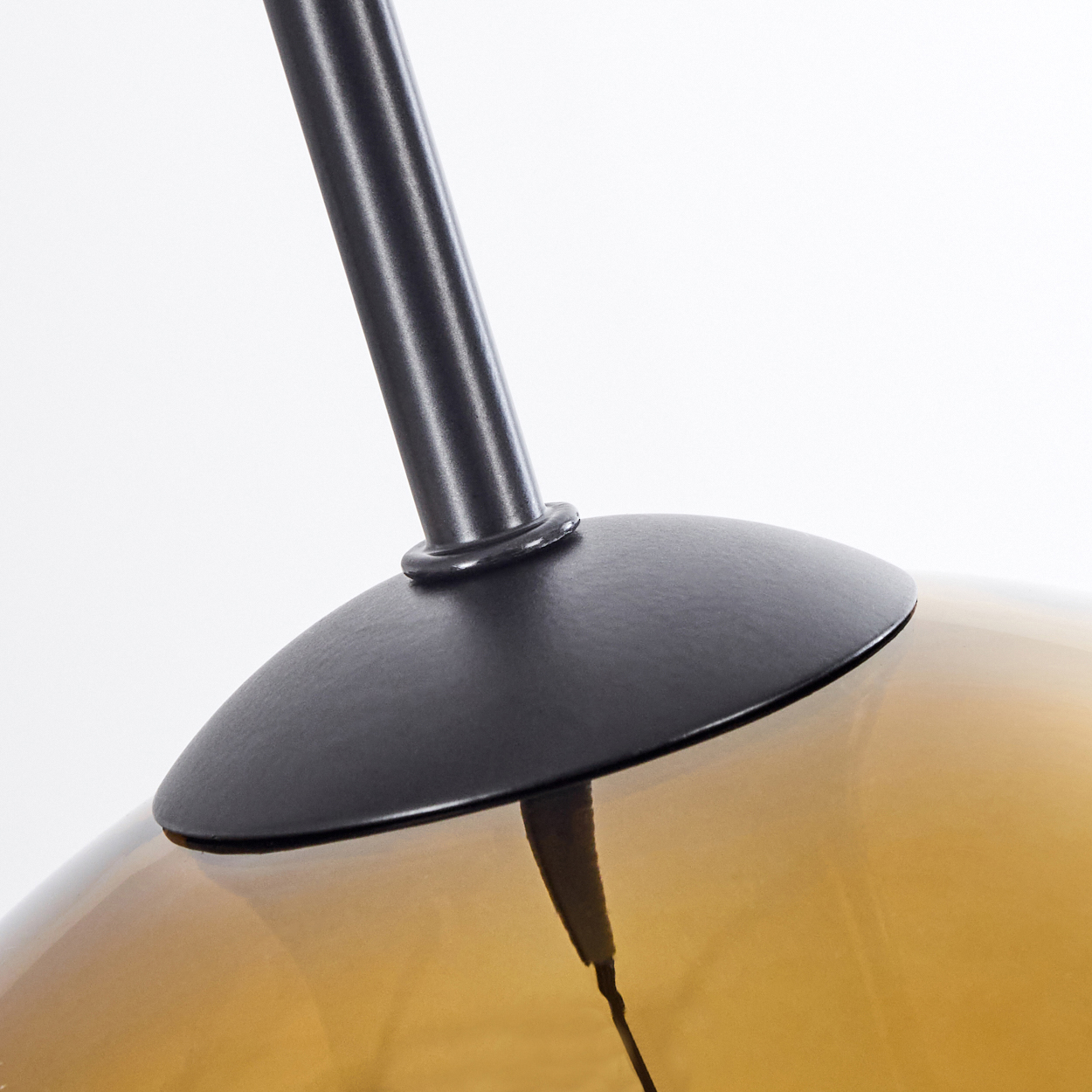 Nahaufnahme einer Lampe. Schwarzer Metallschaft und Schirm tragen einen abgerundeten, bernsteinfarbenen Glasschirm. Weißer Hintergrund.