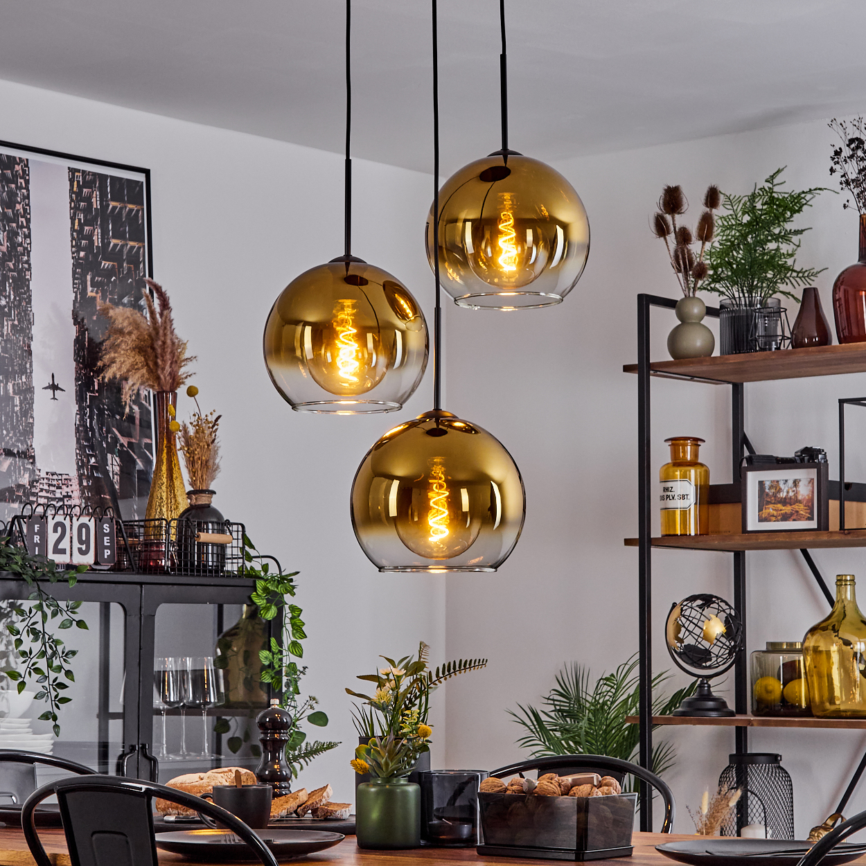 Drei goldene Pendelleuchten über einem Esstisch. Im Hintergrund Regale und ein Schrank.