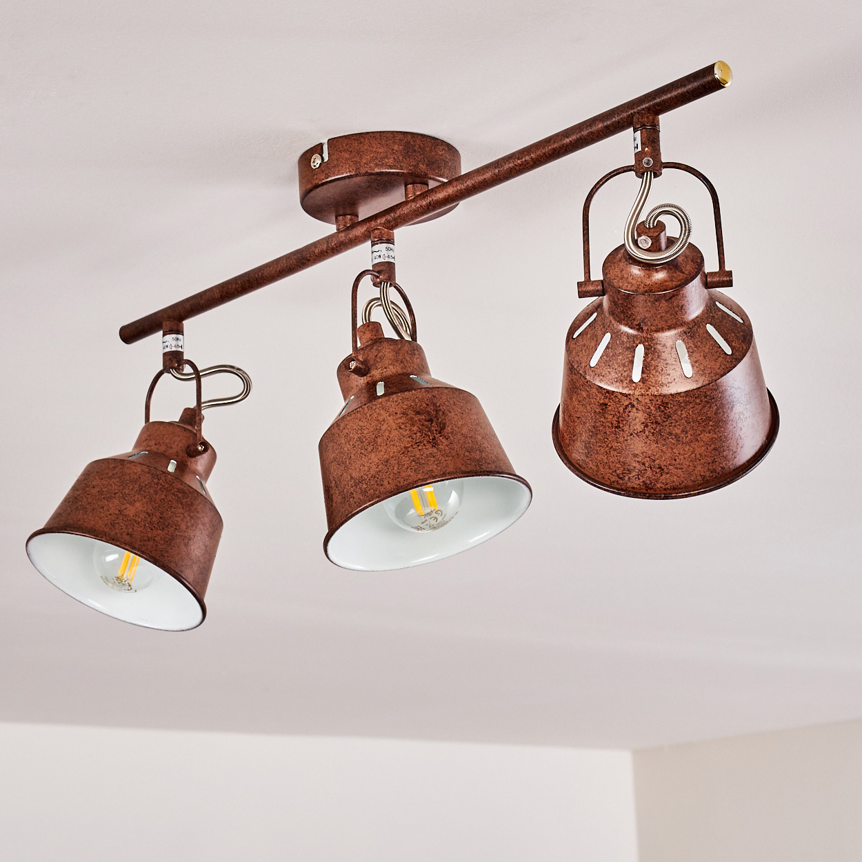 Deckenleuchte mit drei Lampen. Die Lampenschirme sind rostbraun und innen weiß. Der Hintergrund ist eine weiße Decke.