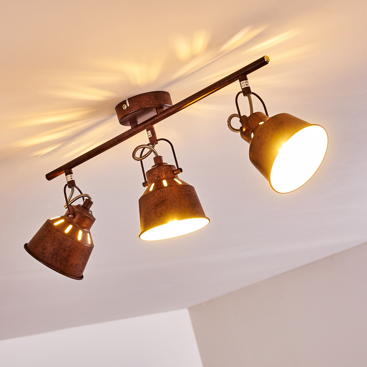 Drei rostbraune Strahler an einer Decke. Jeder Strahler strahlt helles Licht aus. Die Decke ist weiß.