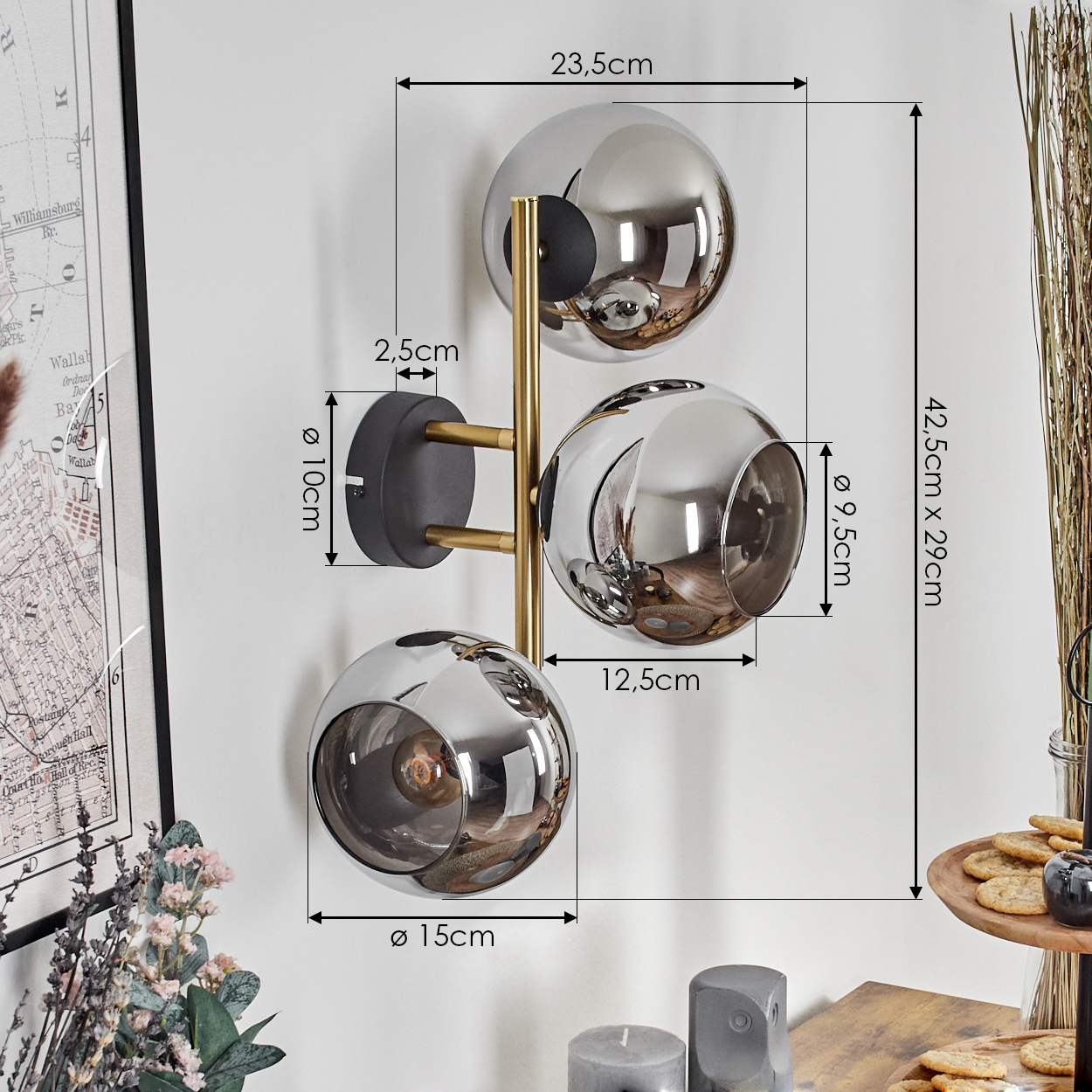 Eine moderne Wandlampe mit drei kugelförmigen Schirmen. Die Lampe hat ein goldfarbenes Gestell und ist an einer weißen Wand befestigt.
