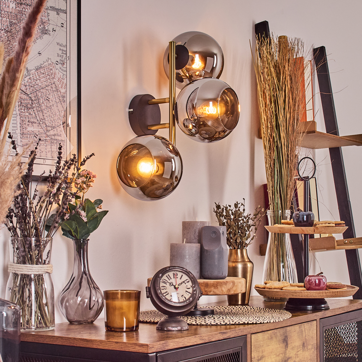 Eine dekorative Szene mit einer Wandlampe, Vasen, Kerzen, einer Uhr und einem Holzregal mit Keksen und Äpfeln.