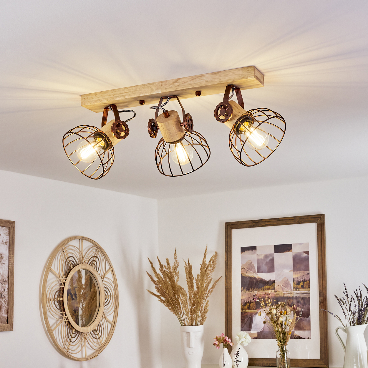 Deckenleuchte mit drei Lampen. Dekorative Metallkäfige um die Glühbirnen, Holzsockel. Weiße Wände, Deko, Spiegel und gerahmte Kunst.