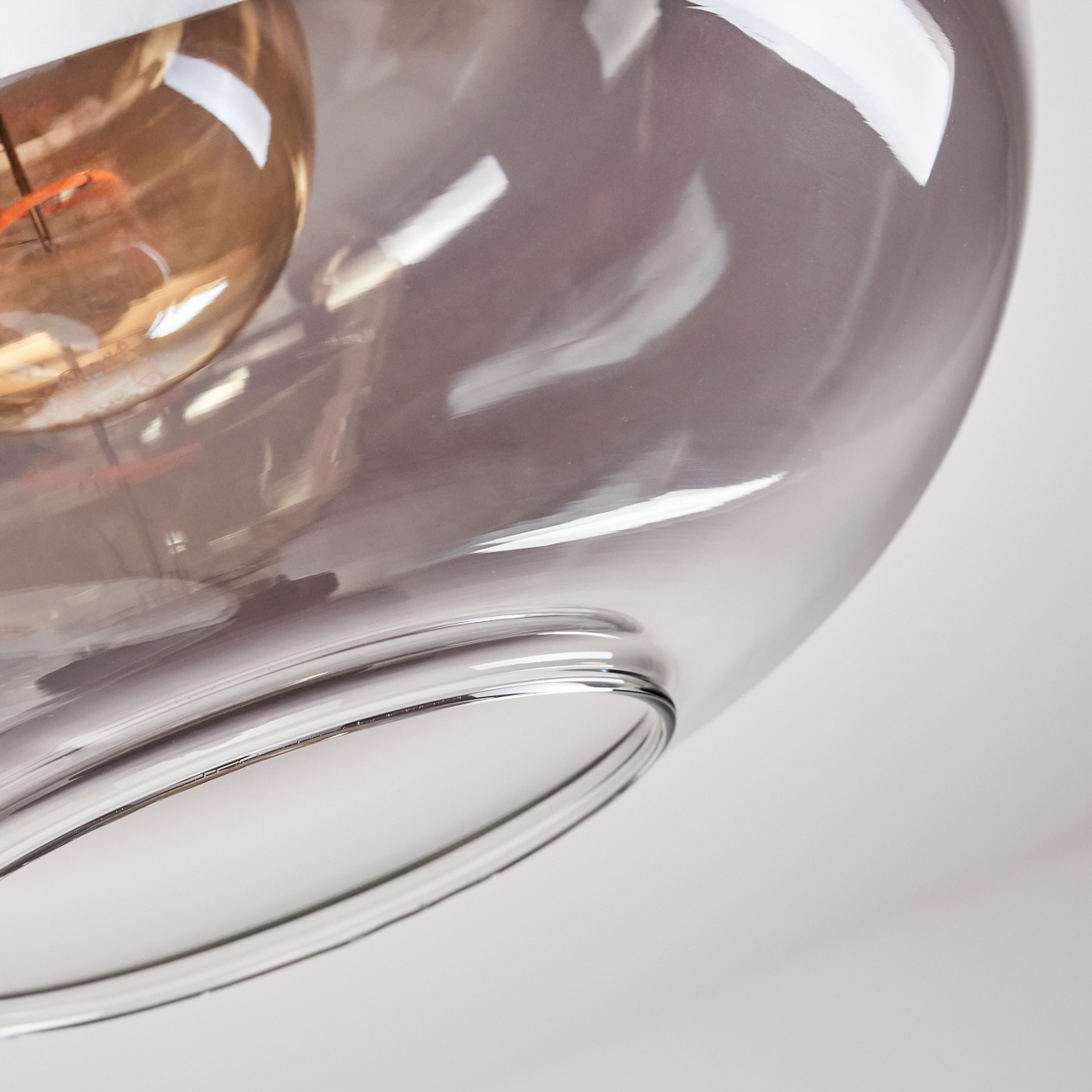 Nahaufnahme einer Glasleuchte. Sie ist transparent und hat eine Glühbirne im Inneren. Der Hintergrund ist weiß.