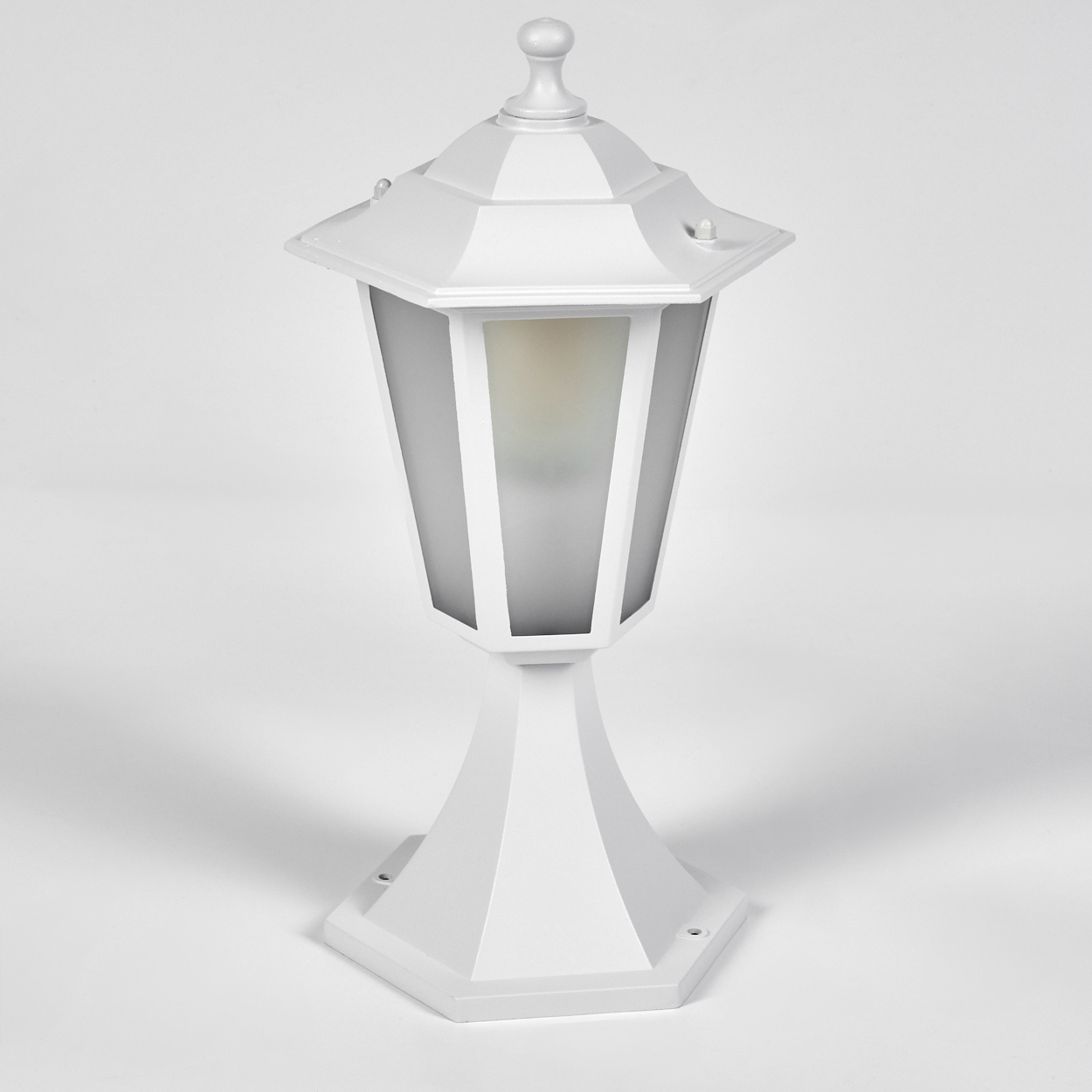 Eine weiße Außenlampe auf weißem Untergrund. Sie hat einen sechseckigen Sockel, einen Schirm aus Milchglas und eine dekorative Spitze.