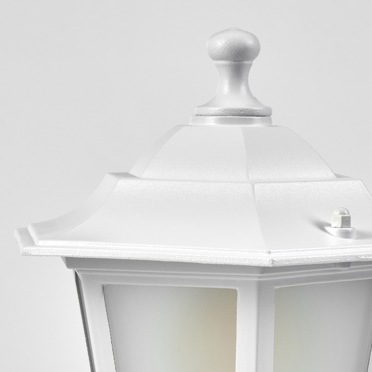 Nahaufnahme einer weißen Außenlampe. Sie hat eine dekorative Oberseite, einen geometrischen Schirm und einen hellen Hintergrund.