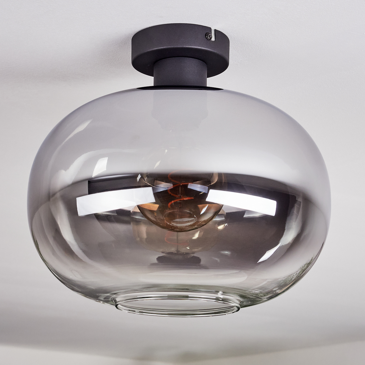 Moderne Deckenleuchte mit großem, grauem, kugelförmigem Glasschirm und dunklem Metallsockel, von einer weißen Decke abgehängt.