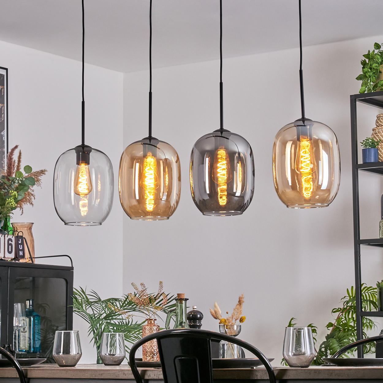 Vier Pendelleuchten mit bernsteinfarbenen und grauen Glasschirmen hängen über einem Tisch. Die Glühbirnen leuchten warm.