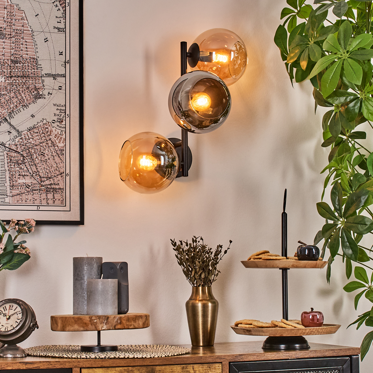 Ein Raum mit Wandlampe, Karte, Uhr, Kerzen, Vase, mehrstöckigem Tablett mit Keksen und Pflanzen.