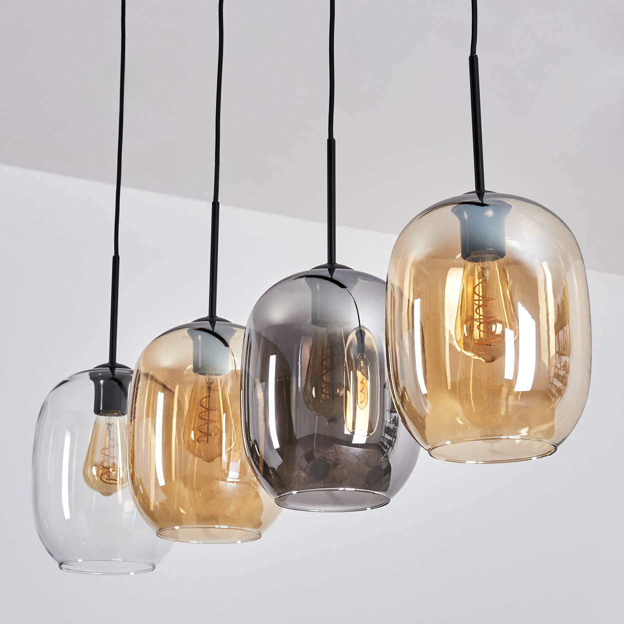 Vier Glas-Pendelleuchten. Jede hat einen anderen Farbton. Sie hängen von der Decke, mit sichtbaren Glühbirnen.